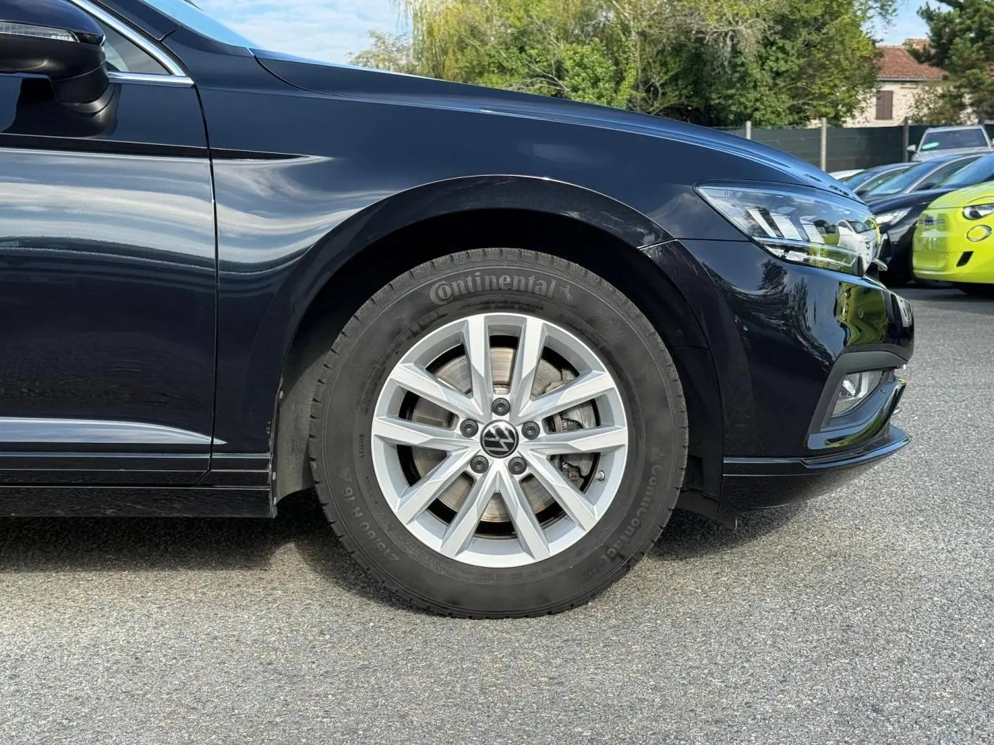 Gros plan sur la roue avant droite et partie avant d'une Volkswagen Passat SW noire nacrée, avec jante alu et phare LED visible.