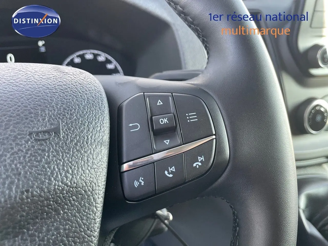Gros plan sur les commandes au volant noir du Ford Transit Fourgon blanc, avec tableau de bord et console en arrière-plan.