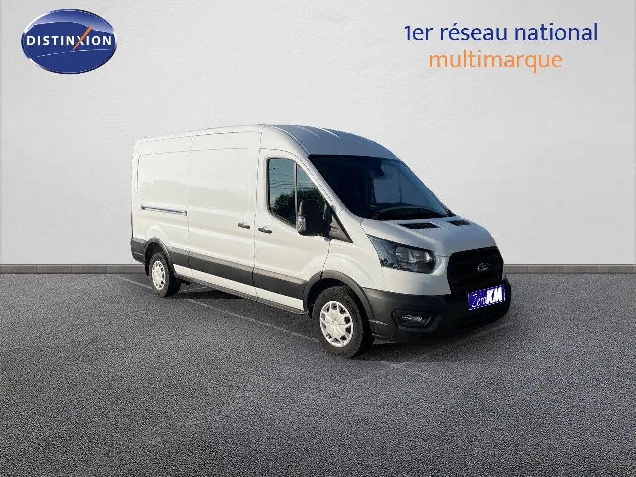 Fourgon Ford Transit blanc en 3/4 avant droit, avec pare-chocs noirs et jantes acier, stationné devant un mur blanc.