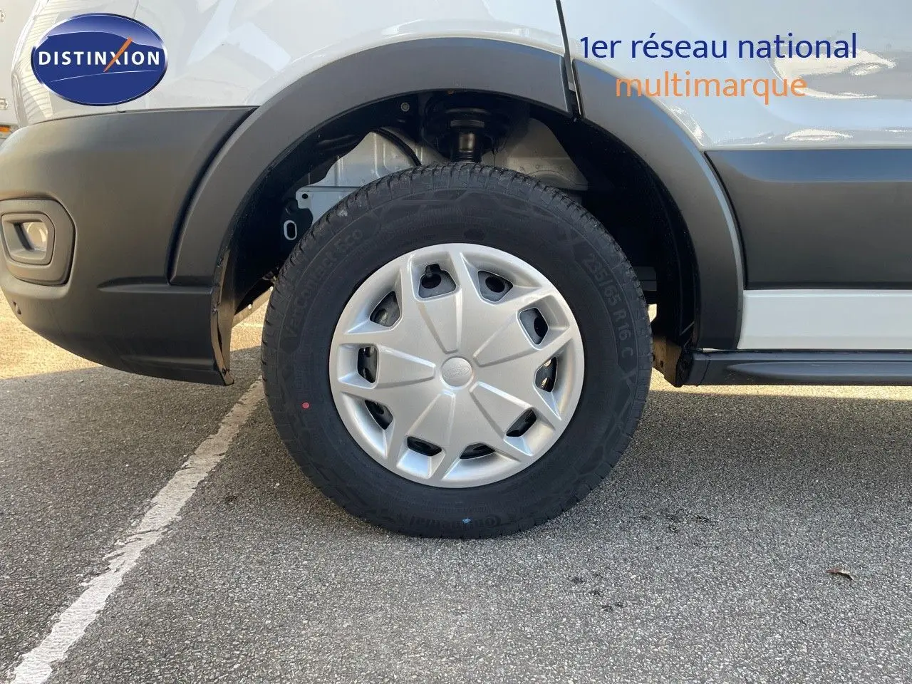 Gros plan sur la roue avant gauche d’un fourgon Ford Transit blanc, soulignant la jante et le pneu.