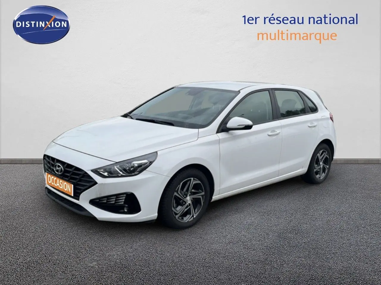 Hyundai i30 blanc nacré vue 3/4 avant droit, compacte 5 portes avec jantes alliage et calandre noire distinctive.