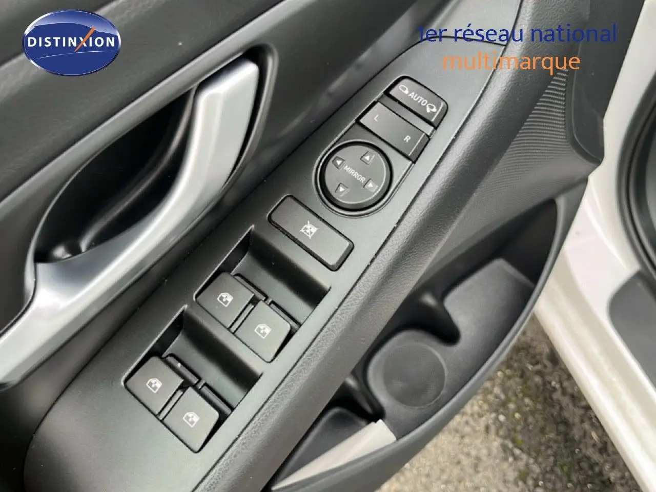 Gros plan sur la commande des vitres et rétroviseurs côté conducteur d'une Hyundai i30 blanc nacré 2023.