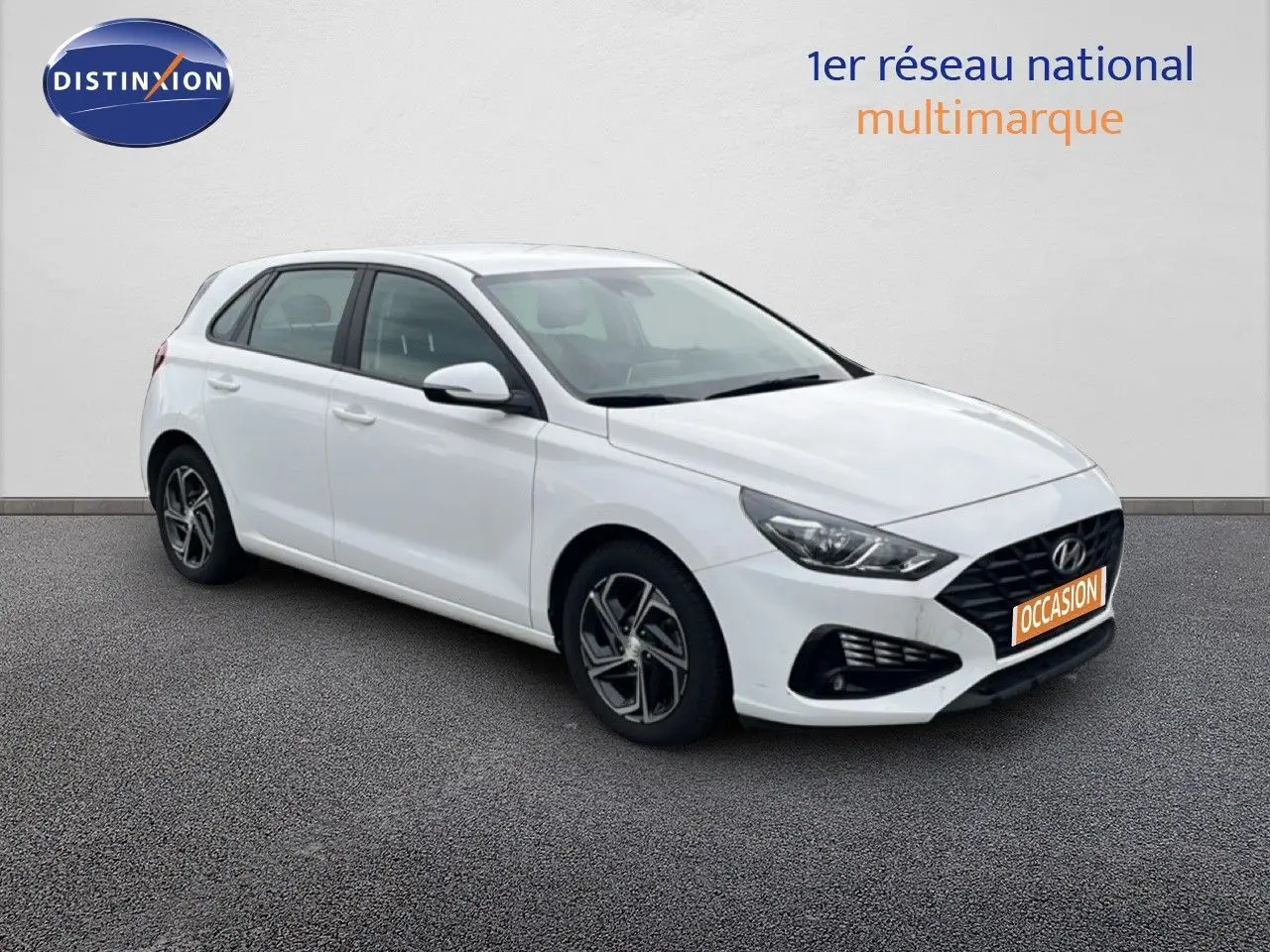 Vue 3/4 avant droit d'une Hyundai i30 blanche nacrée 5 portes, avec jantes alliage et calandre noire distinctive.