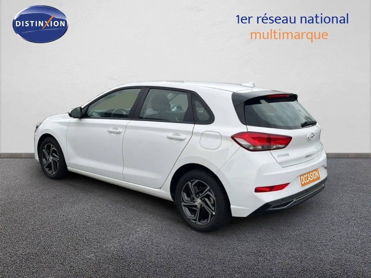Vue 3/4 arrière droite d'une Hyundai i30 blanche nacrée 2023, compacte 5 portes avec jantes alliage et feux arrière LED.