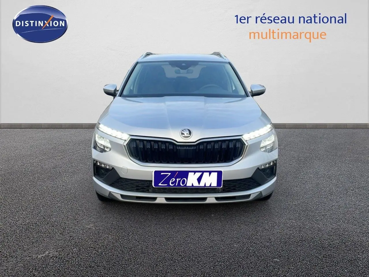 Vue frontale d'un Skoda Kamiq gris argent métal avec calandre noire et feux LED allumés sur fond neutre.