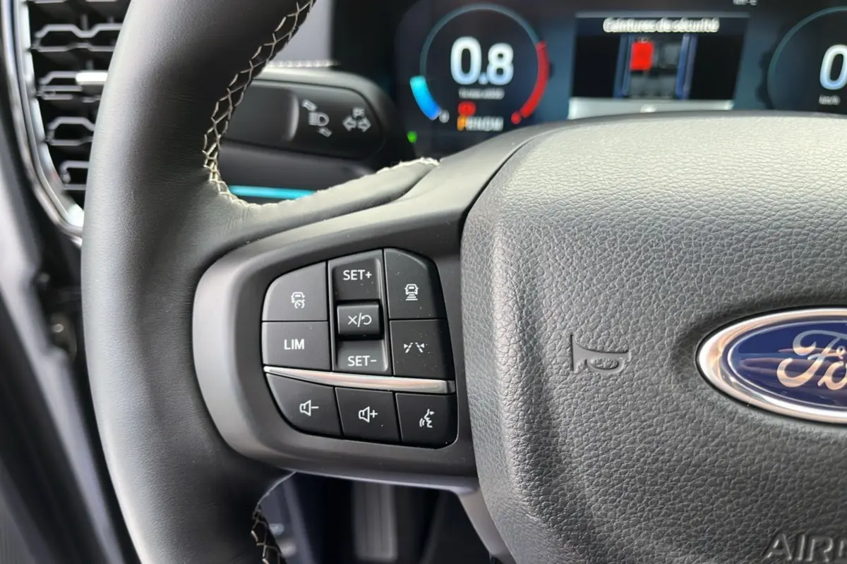 Gros plan sur le volant cuir multifonctions du Ford Ranger gris iconic, avec commandes de régulateur et affichage numérique en arrière-plan.