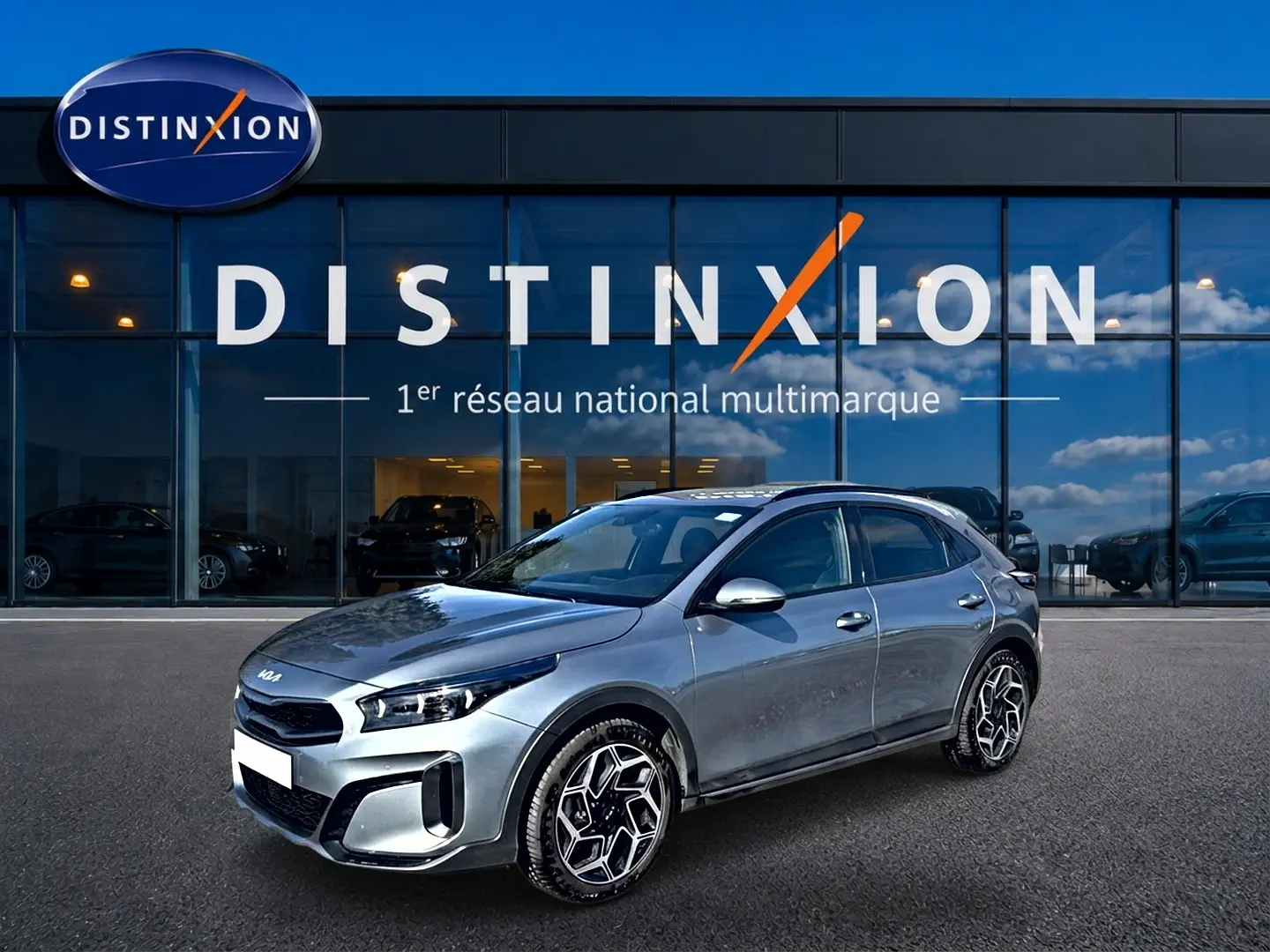 KIA Xceed gris en 3/4 avant droit, avec jantes alu distinctives, stationné devant une vitrine Distinxion.