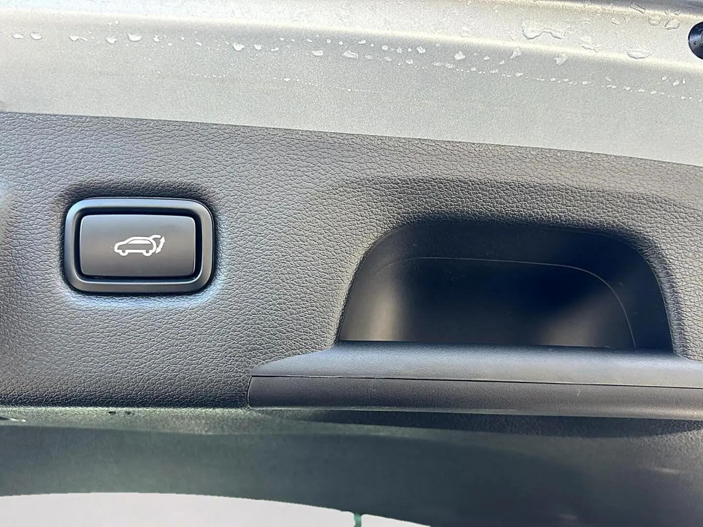 Bouton d'ouverture électrique du coffre sur la garniture intérieure noire du hayon d'un KIA Xceed gris 2024.