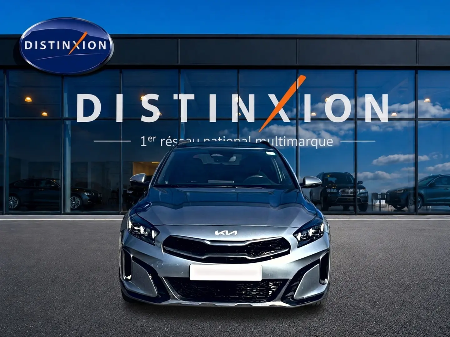 Vue frontale d'une KIA Xceed gris métallisé avec calandre chromée et feux LED, devant une vitrine Distinxion.