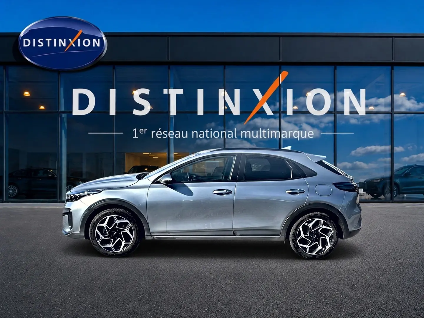 Vue latérale droite d'un KIA Xceed gris 2024 avec jantes alliage au design géométrique devant un showroom Distinxion.