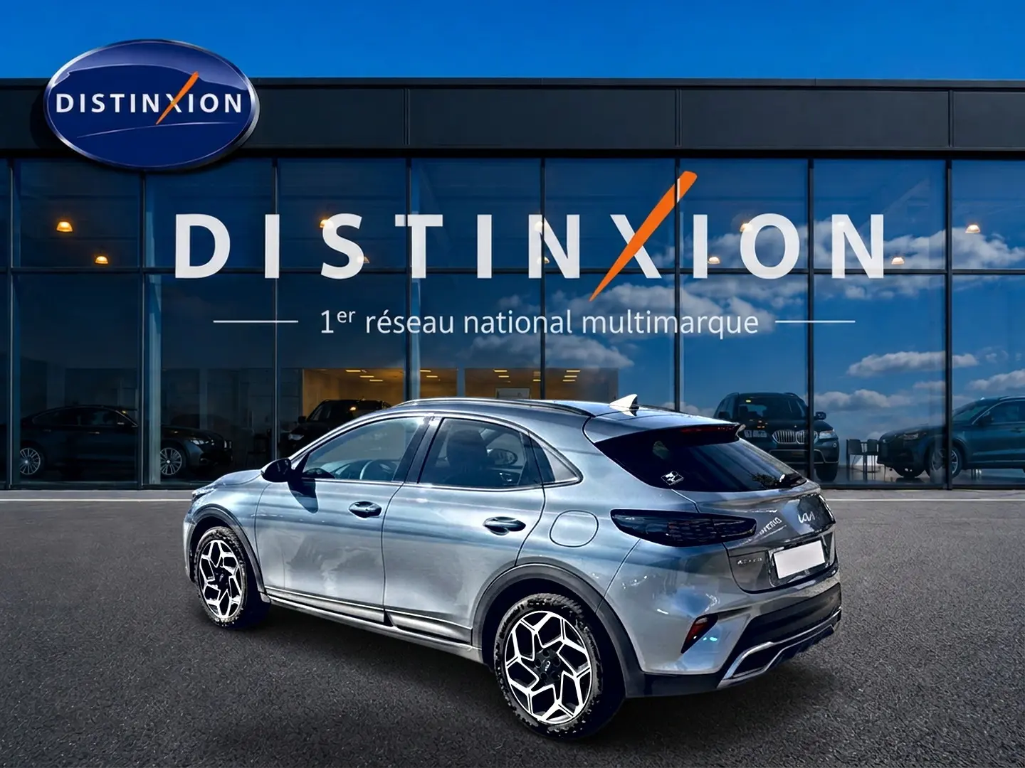 Vue 3/4 arrière droite d'un KIA Xceed gris 2024 avec jantes alu et becquet arrière, devant une vitrine Distinxion.