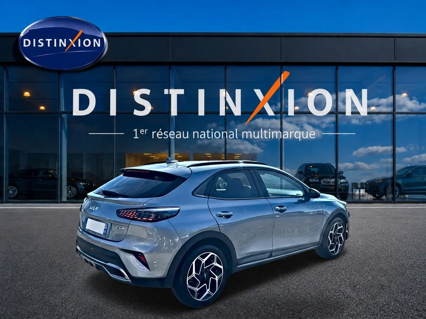 Vue 3/4 arrière droite d'un KIA Xceed gris 2024 avec jantes alu et becquet arrière, devant une vitrine Distinxion.