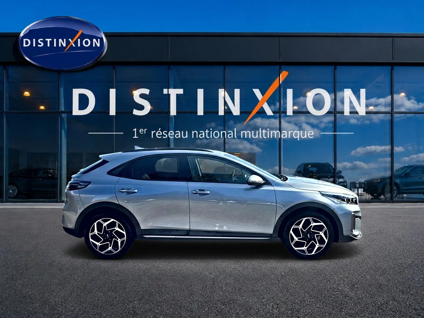 KIA Xceed gris en profil droit, avec jantes alu distinctives et calandre chromée visible devant un showroom Distinxion.