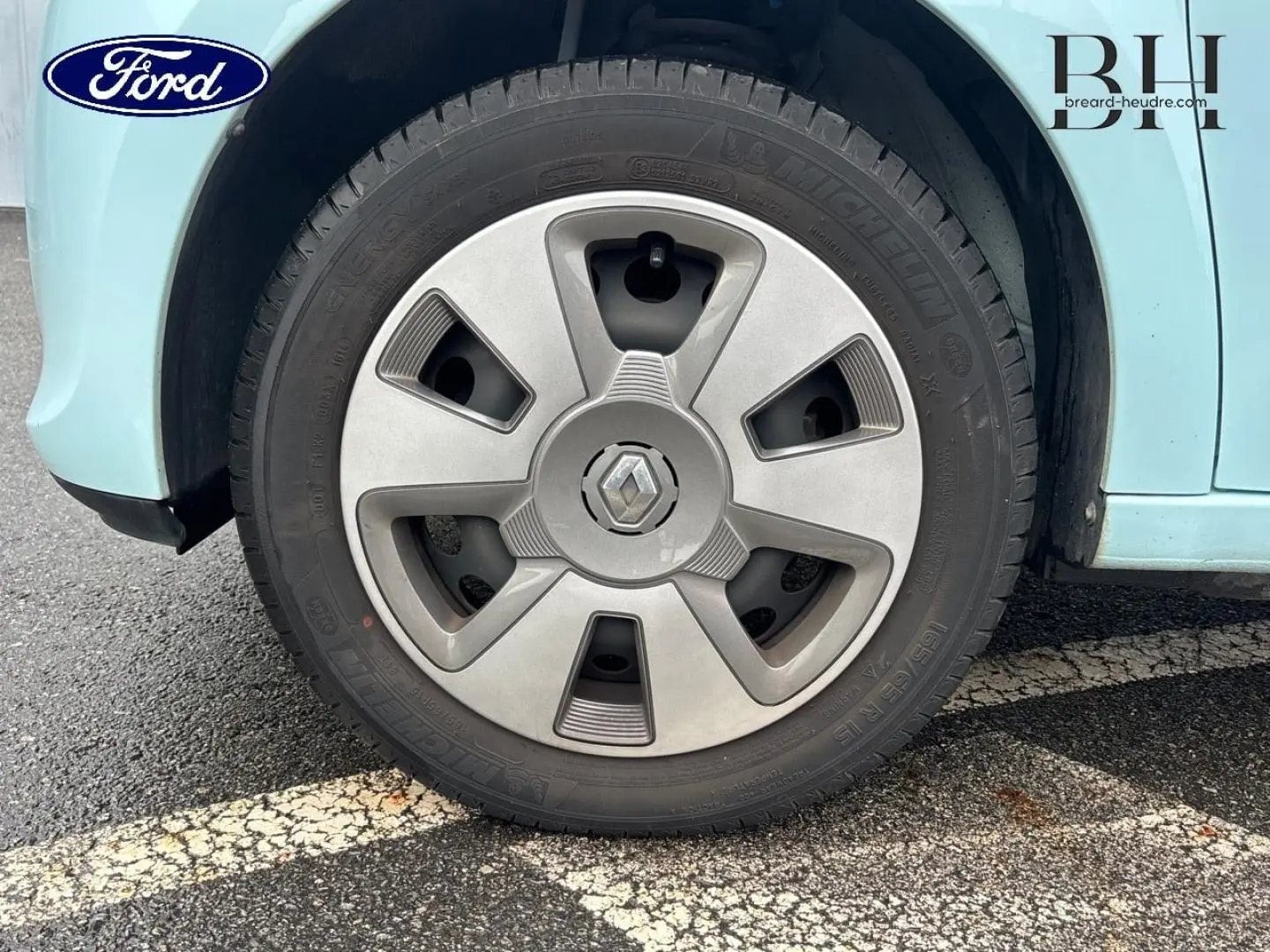 Gros plan sur la roue avant gauche d'une Renault Twingo bleu dragée avec jante en alliage gris.