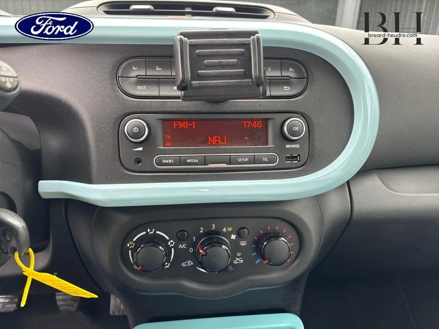 Tableau de bord intérieur d'une Renault Twingo bleu dragée 2014, avec commandes clim manuelle et radio affichant NRJ.