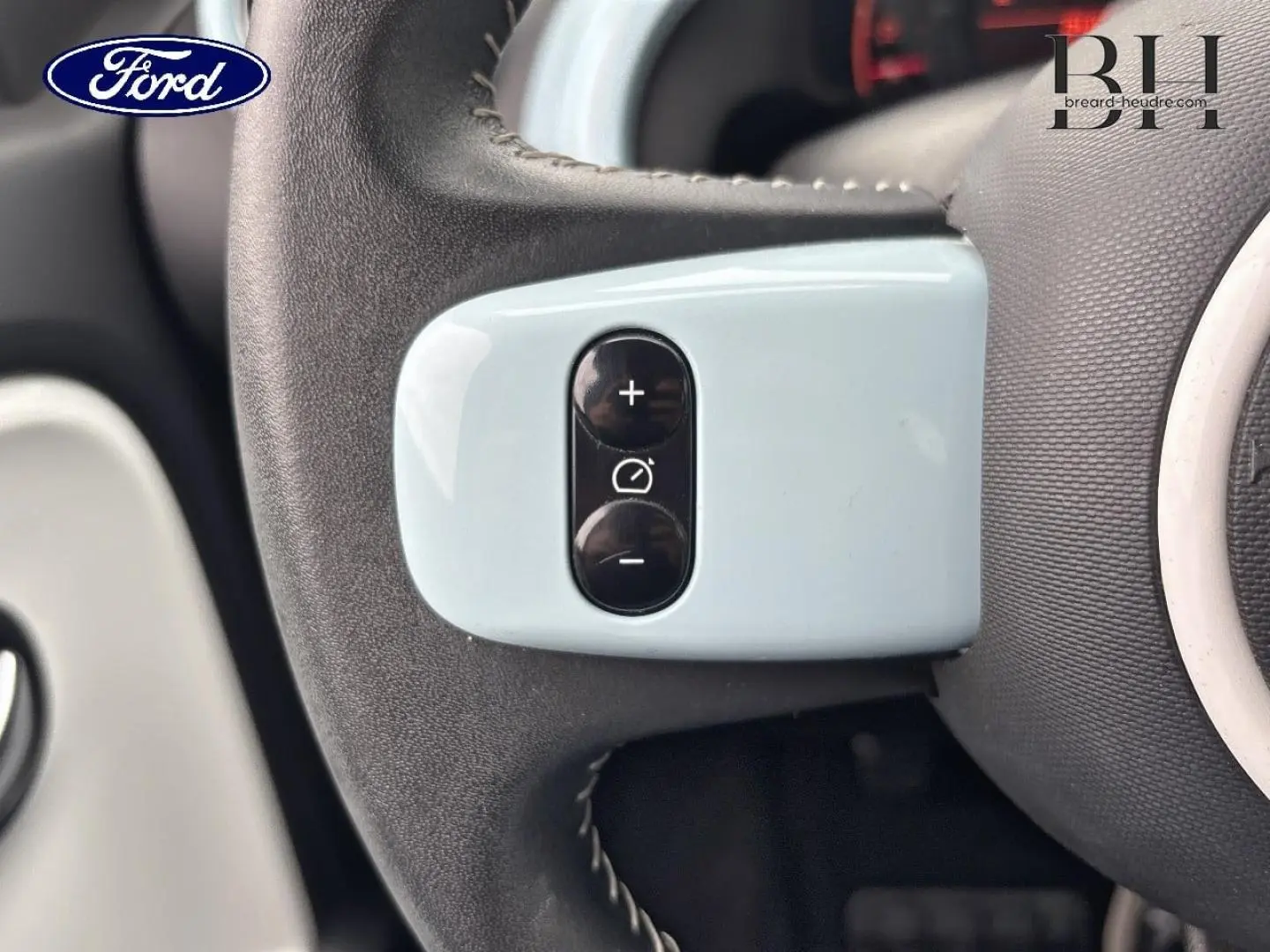 Gros plan sur les commandes de régulateur de vitesse sur le volant bleu dragée de la Renault Twingo 2014.
