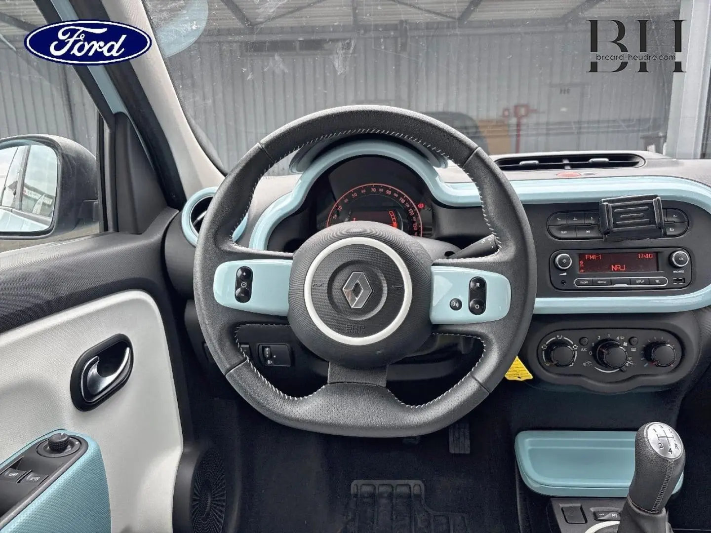 Vue intérieure centrée sur le volant et le tableau de bord bleu dragée de la Renault Twingo 2014 avec boîte manuelle.