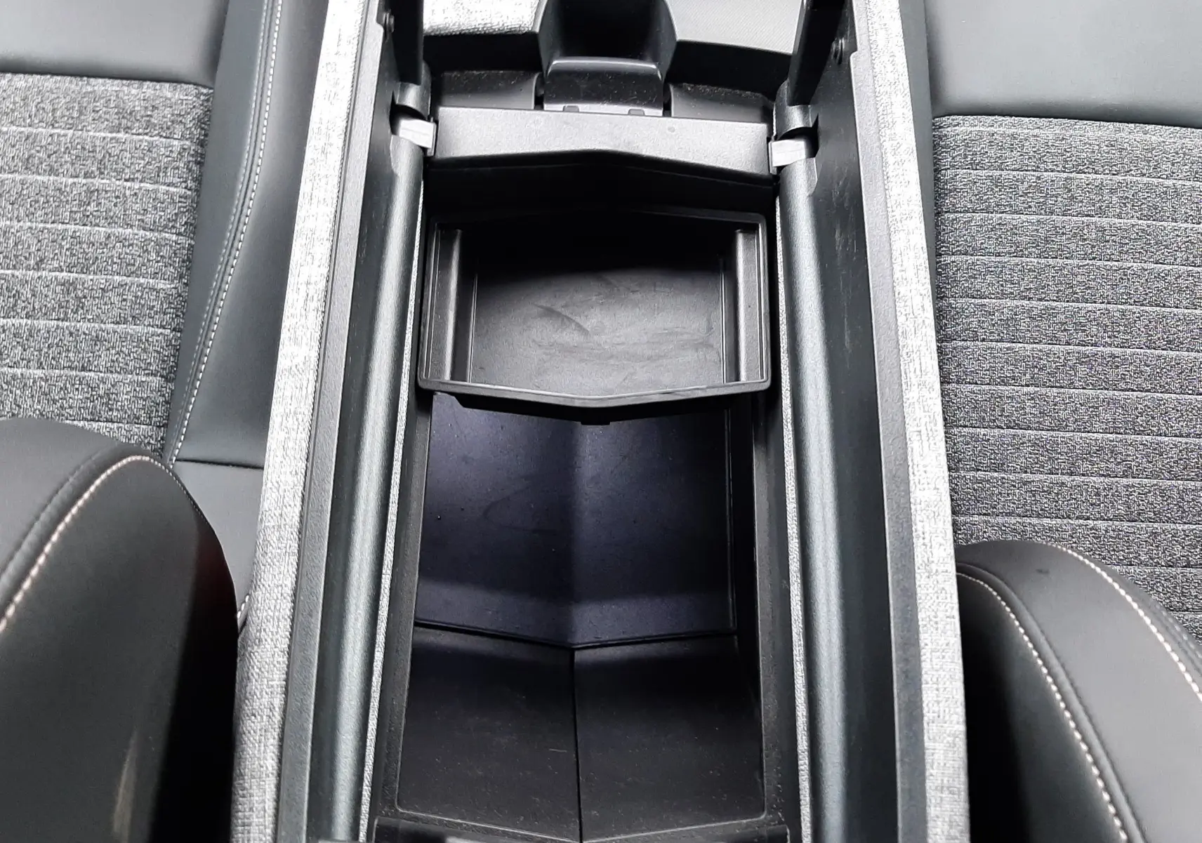 Vue plongeante sur le rangement central ouvert entre les sièges gris et noir du Peugeot 3008 III HYBRID 145 ALLURE 2025.