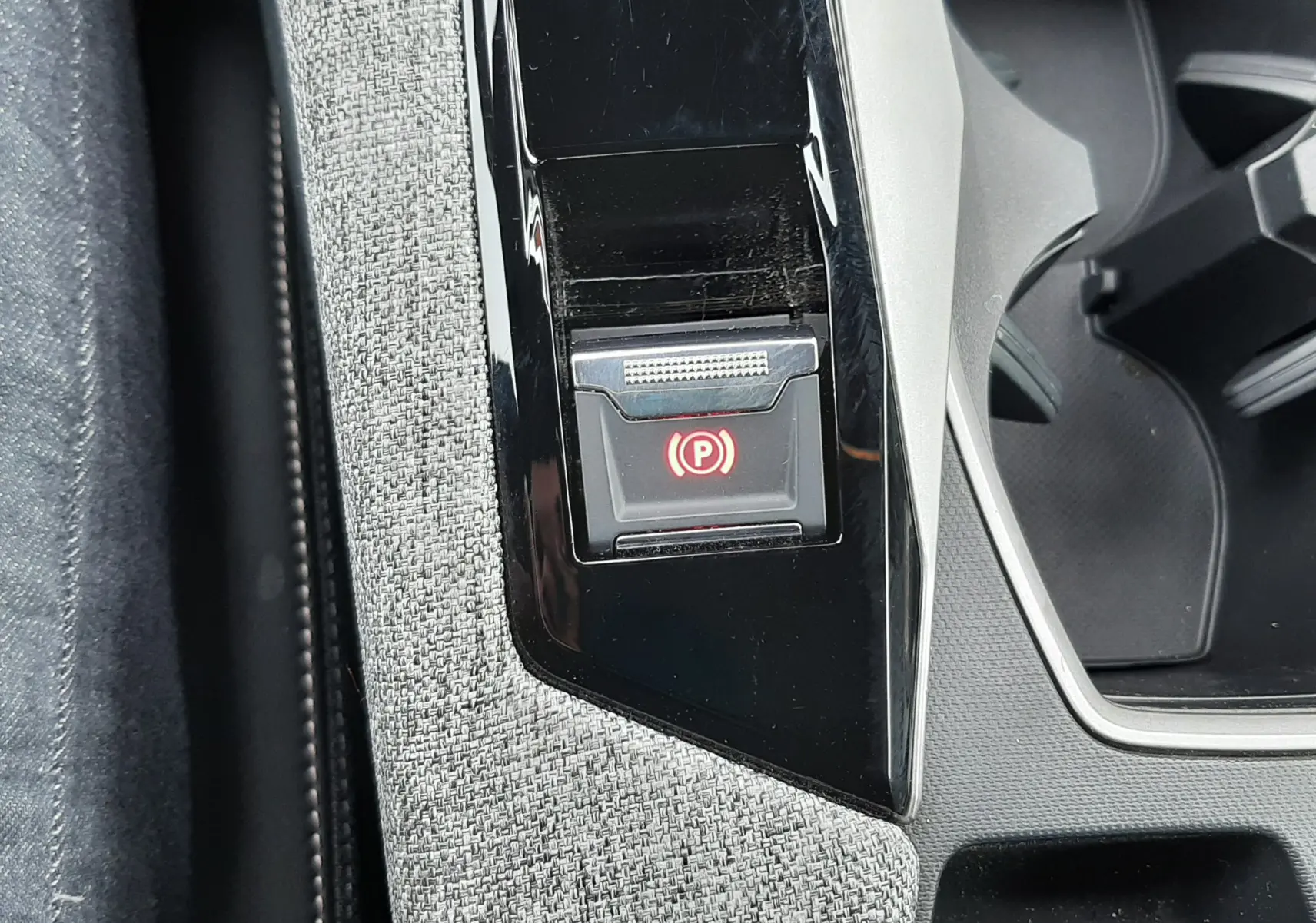 Gros plan sur le bouton de frein à main électronique rouge, entouré de garniture grise et console noire du Peugeot 3008 hybride 2025.