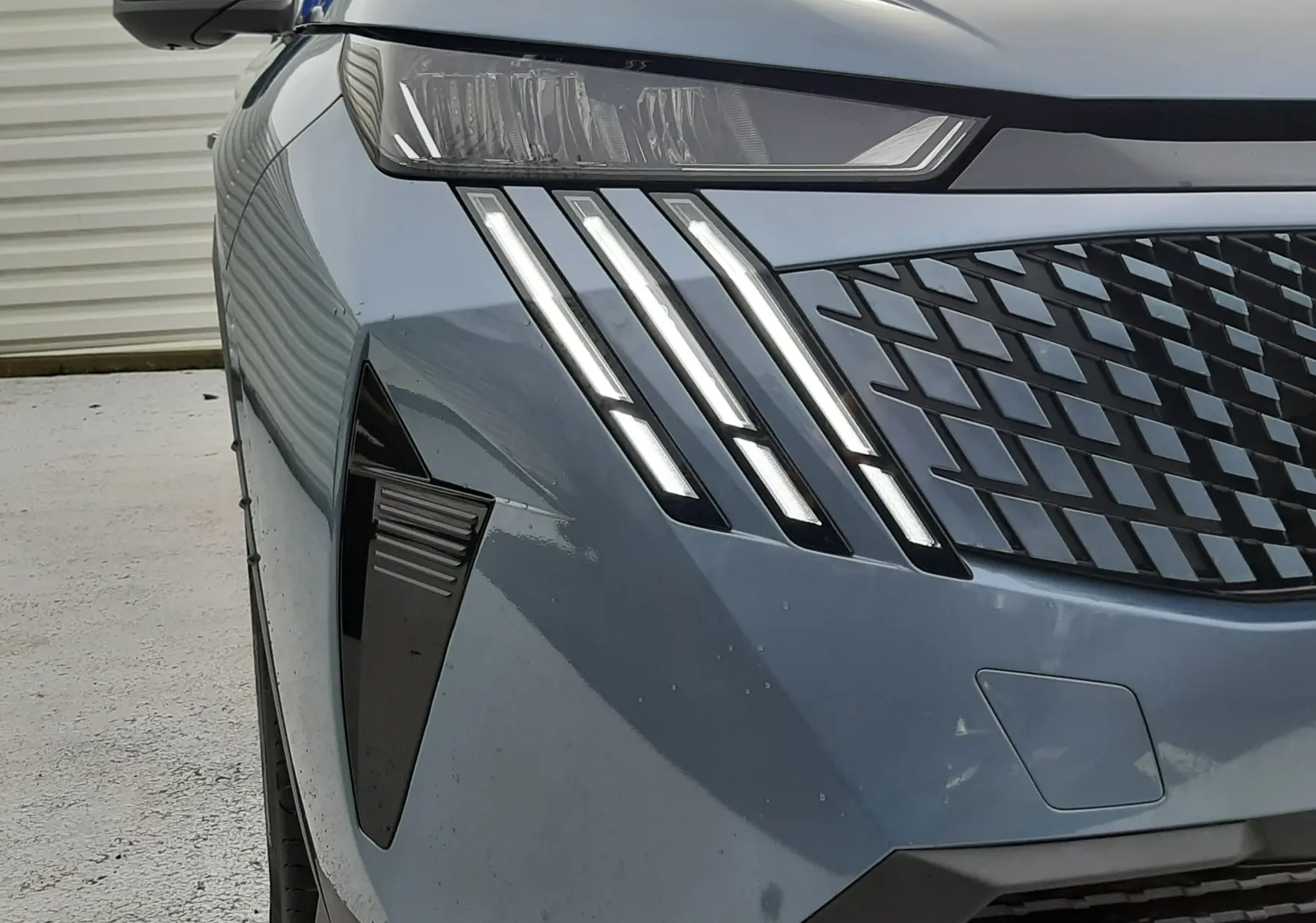 Vue avant gauche rapprochée du Peugeot 3008 III Hybrid bleu Ingaro, mettant en valeur ses phares LED et sa calandre distinctive.