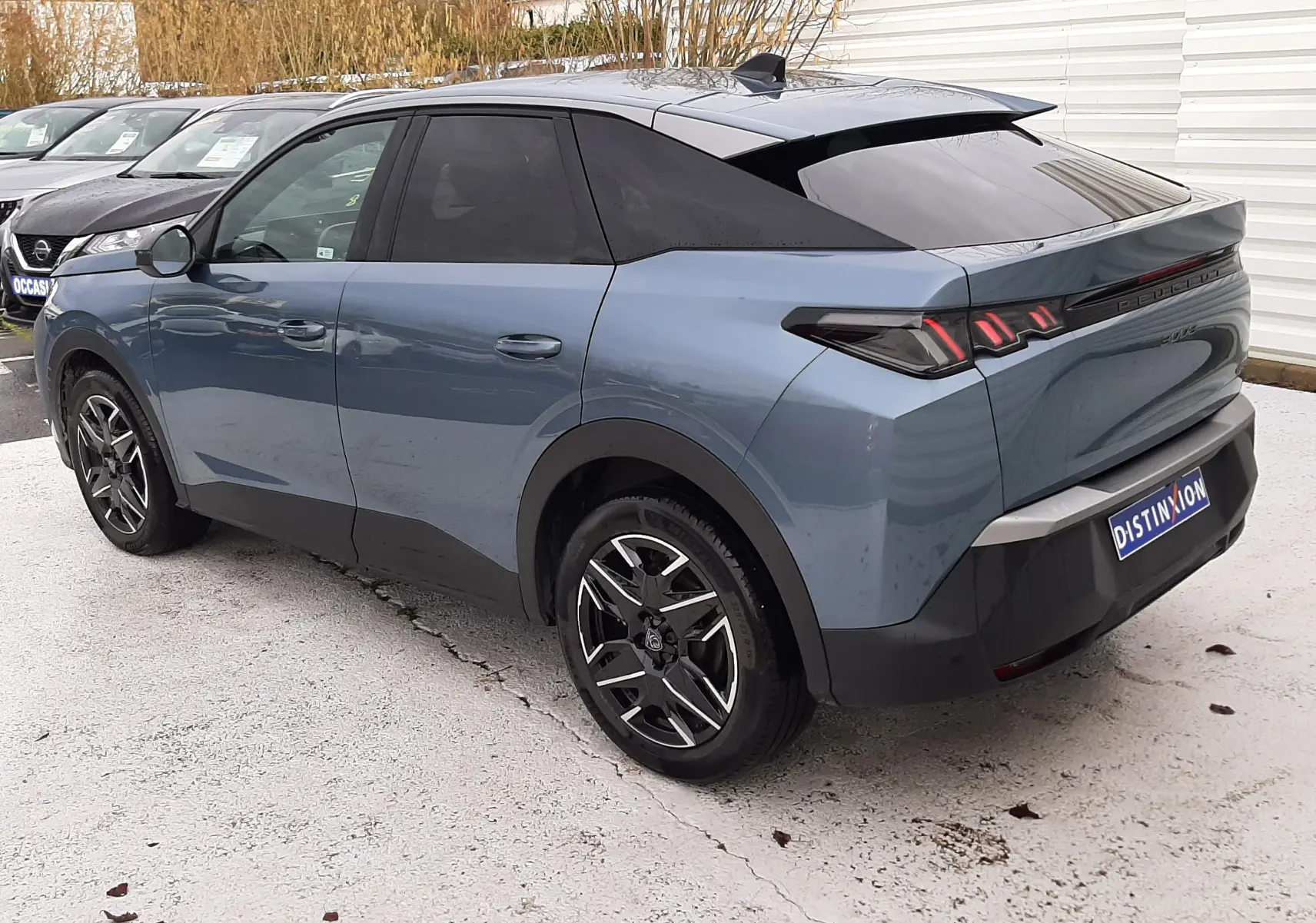 Vue 3/4 arrière droite d’un Peugeot 3008 HYBRID bleu Ingaro avec toit noir et jantes alliage bicolores.