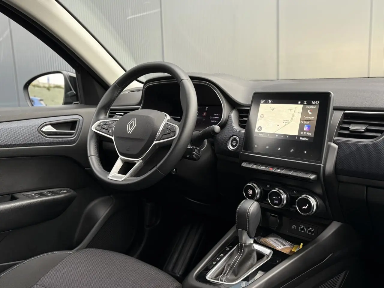 Vue intérieure côté conducteur du Renault Arkana bleu Zanzibar, avec volant multifonction, écran tactile GPS et levier de boîte auto.