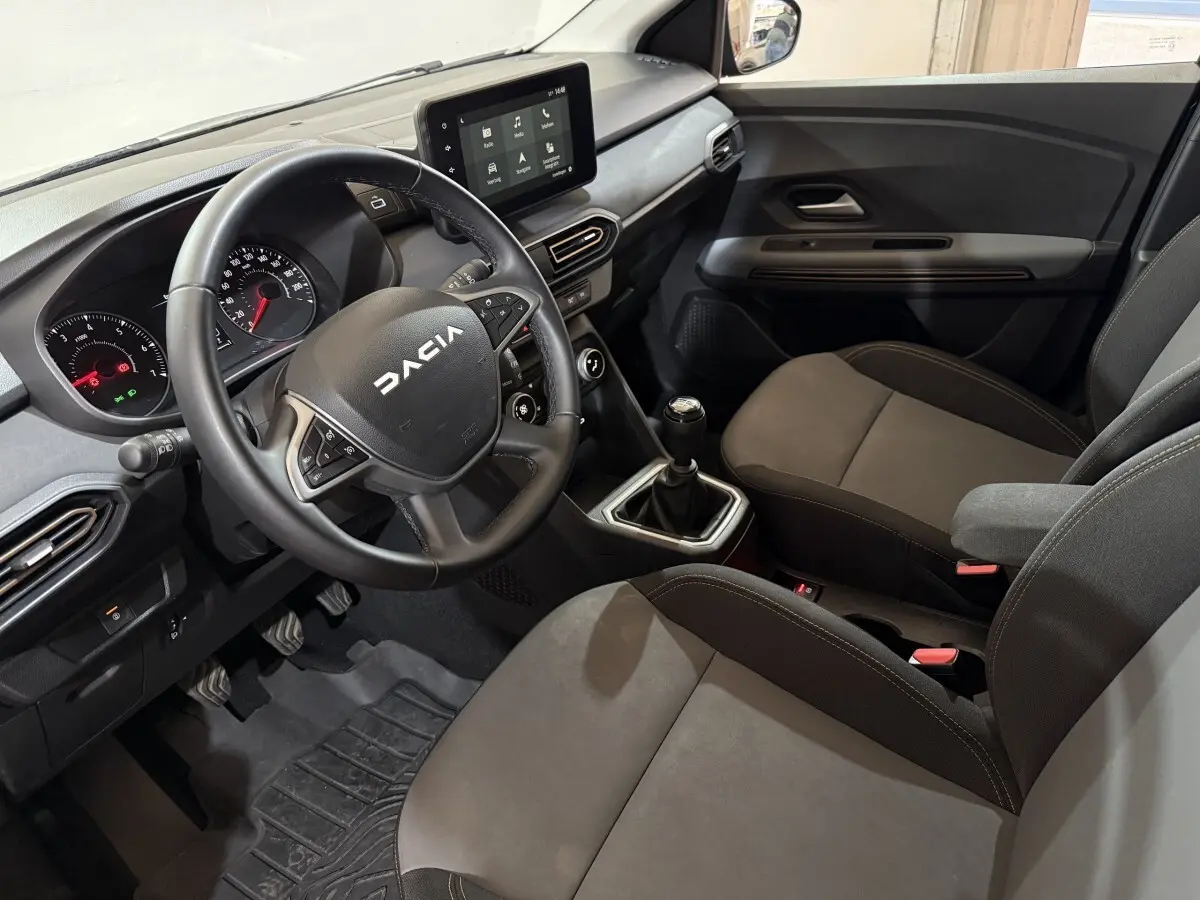 Vue intérieure côté conducteur de la Dacia Sandero 2024, volant cuir multifonctions et écran tactile central visible.