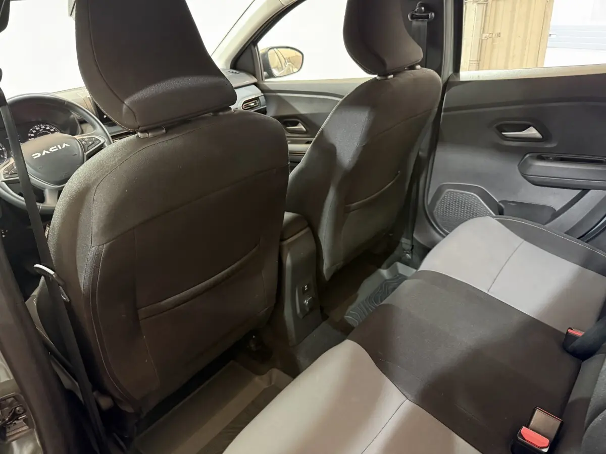 Vue intérieure arrière de la Dacia Sandero 2024, sièges tissu bicolore noir et gris, côté droit avec portes fermées.