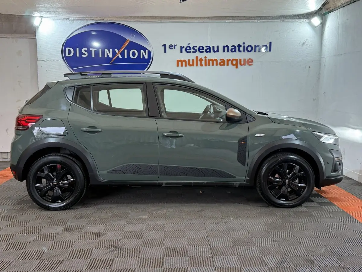 Vue latérale droite d'une Dacia Sandero Extreme+ 2024 verte avec jantes noires et barres de toit assorties.