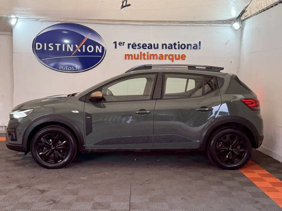 Vue de profil côté gauche d'une Dacia Sandero Extreme+ TCe 110 2024 vert foncé avec jantes noires et barres de toit.