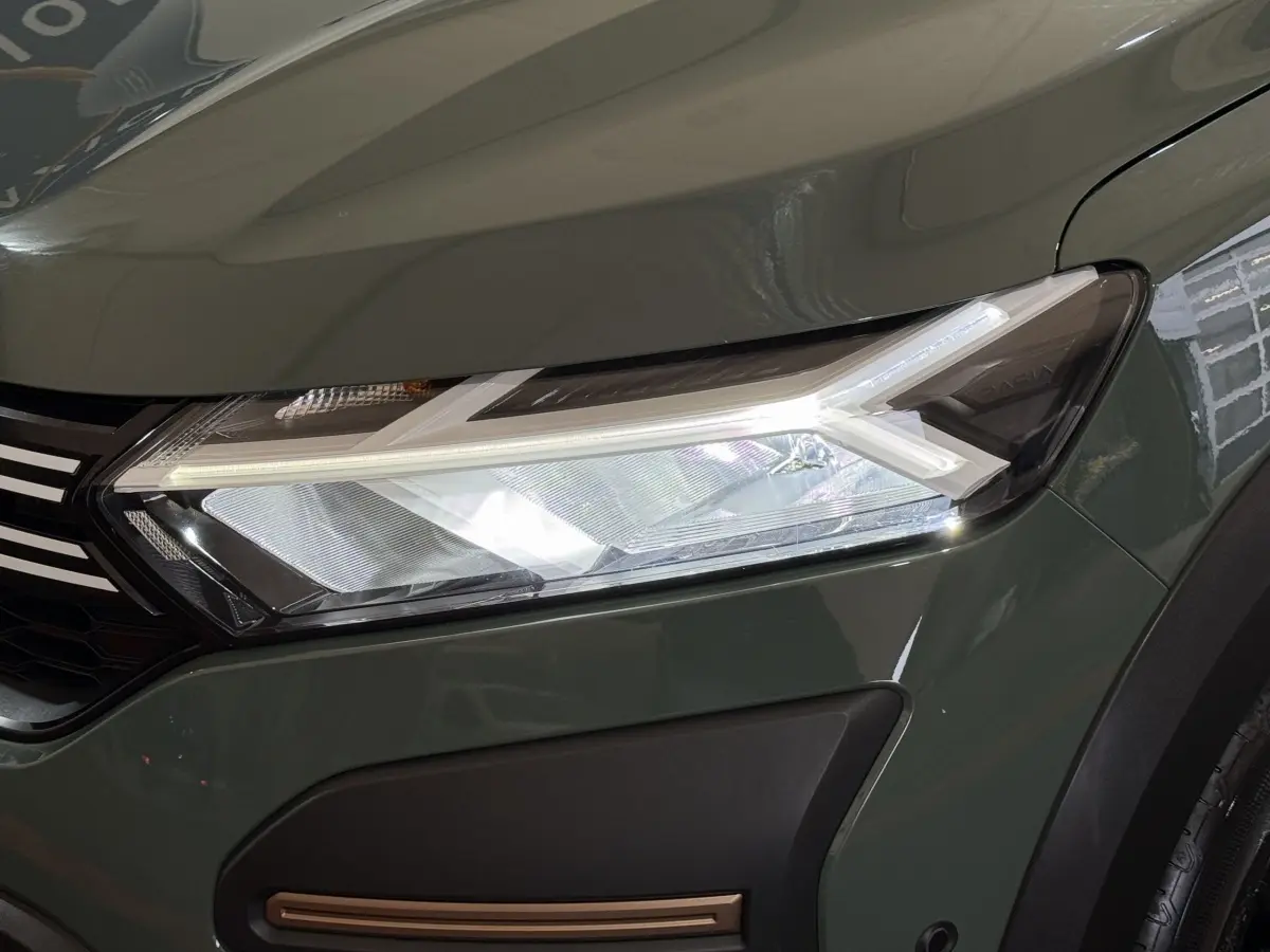 Gros plan sur le phare avant droit LED d'une Dacia Sandero Extreme+ TCe 110 2024 vert foncé avec calandre noire.