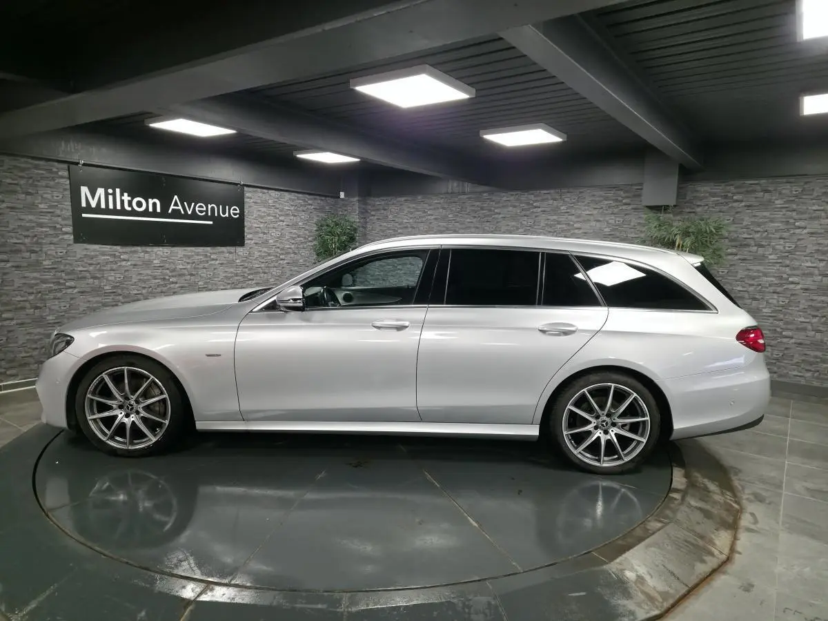 Vue latérale droite d'un break Mercedes Classe E gris métallisé avec jantes AMG 19 pouces dans un showroom intérieur.