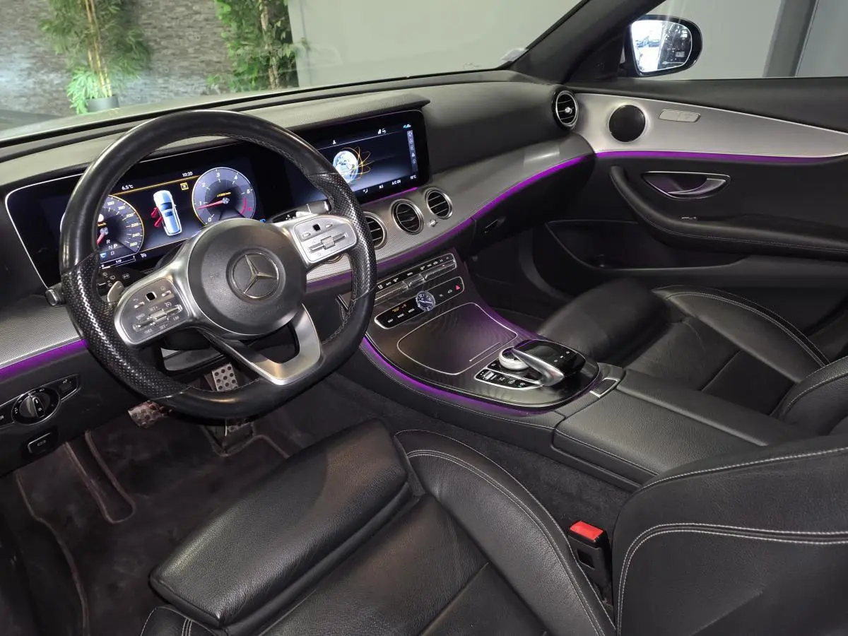 Vue intérieure côté conducteur de la Mercedes Classe E Break 2020, avec éclairage d’ambiance violet et finitions bois brun.