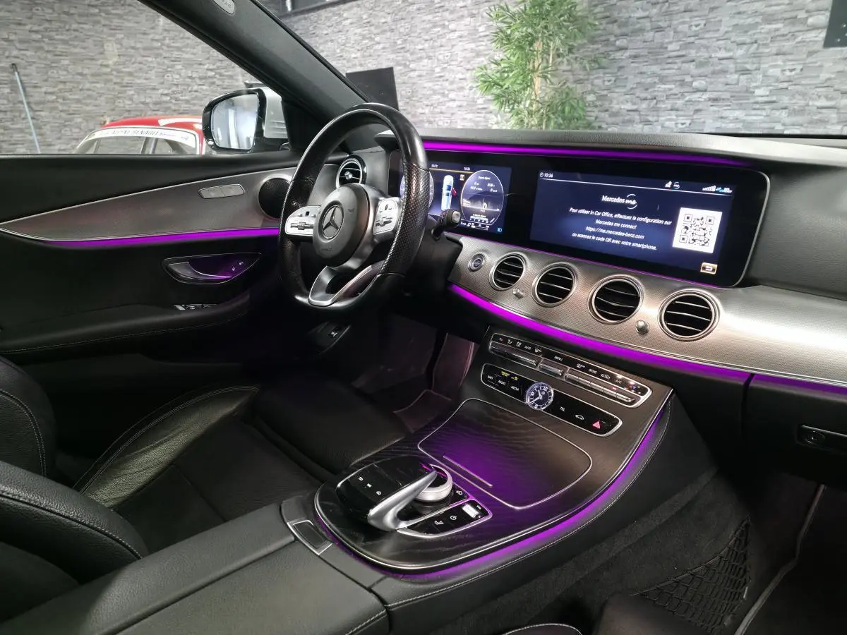 Vue intérieure côté conducteur du Mercedes Classe E Break gris, avec éclairage d'ambiance violet et écran large tactile.