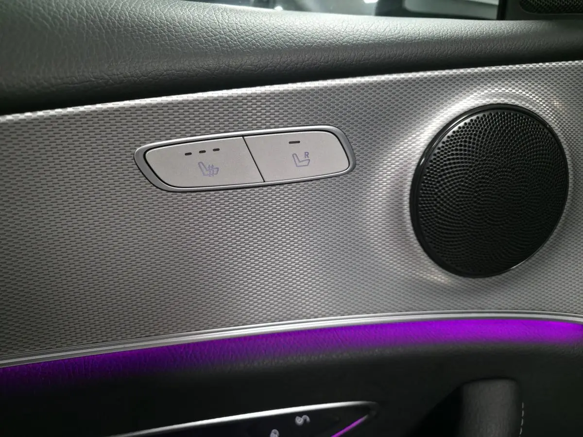 Détail du panneau de porte côté gauche avec haut-parleur rond, commandes de sièges chauffants et éclairage d'ambiance violet.