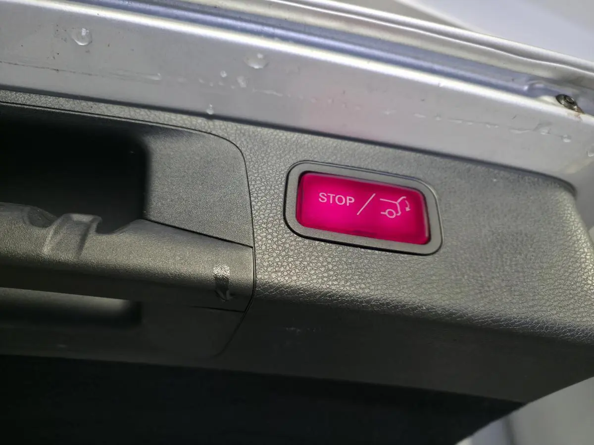 Bouton rouge STOP pour fermeture électrique du hayon sur le bord intérieur du coffre d’un Mercedes Classe E Break gris.