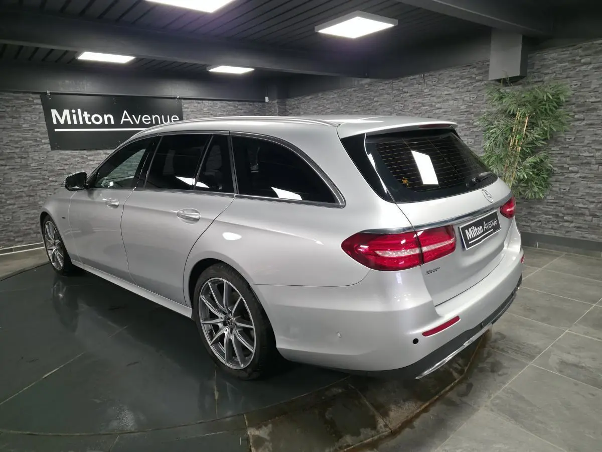 Vue 3/4 arrière droite d'un break Mercedes Classe E gris métallisé avec jantes AMG 19 pouces dans un showroom.
