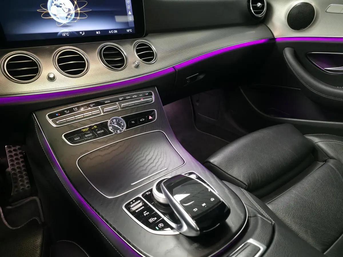 Vue intérieure côté passager du tableau de bord et console centrale noire avec éclairage d'ambiance violet sur Mercedes Classe E Break AMG Line 2020.