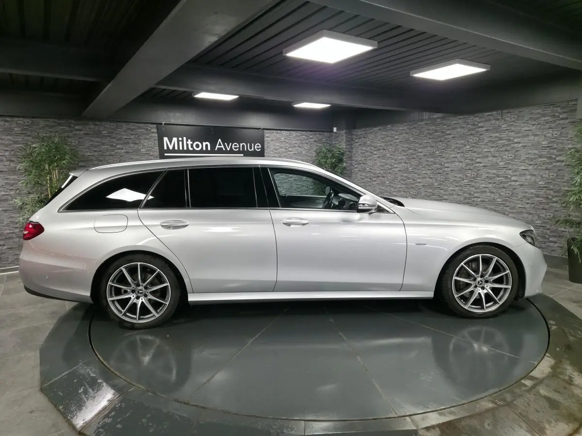 Vue de profil côté gauche d’un break Mercedes Classe E gris métallisé avec jantes AMG 19 pouces dans un showroom.