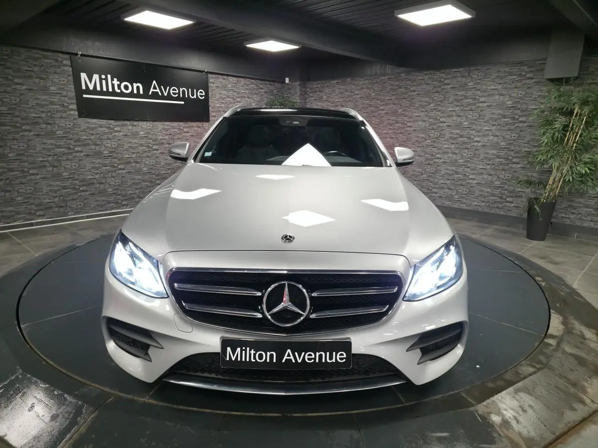 Vue avant d'une Mercedes Classe E Break E 200 d AMG Line gris métallisé avec phares LED allumés en intérieur.