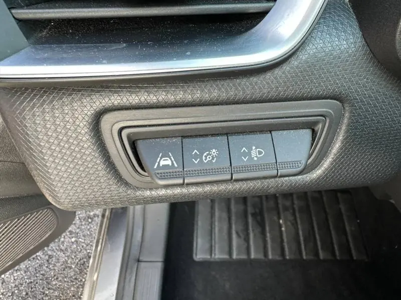 Boutons de réglage des aides à la conduite et des phares sur la partie gauche du tableau de bord d’une Renault Clio gris 2023.