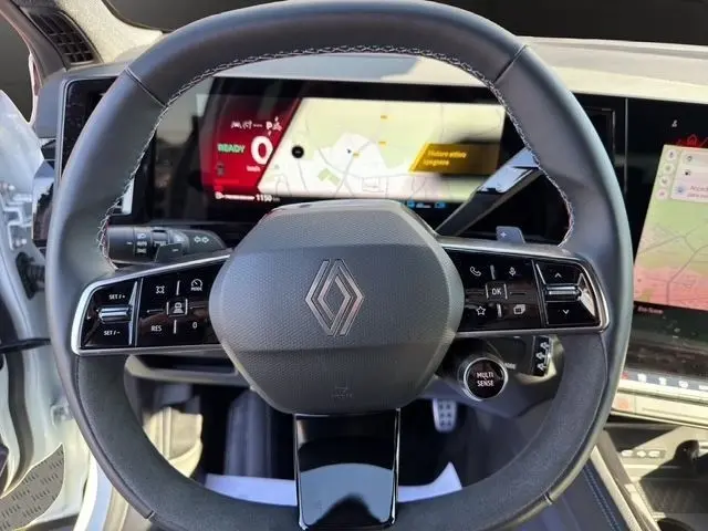 Vue rapprochée du volant cuir noir de la Renault Austral blanc, avec commandes multifonctions et écran tactile en arrière-plan.