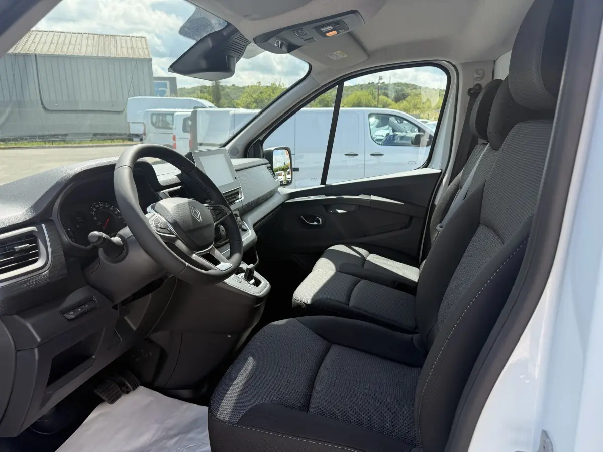 Intérieur vue côté conducteur du Renault Trafic blanc 2025, montrant le volant multifonctions et les sièges noirs.