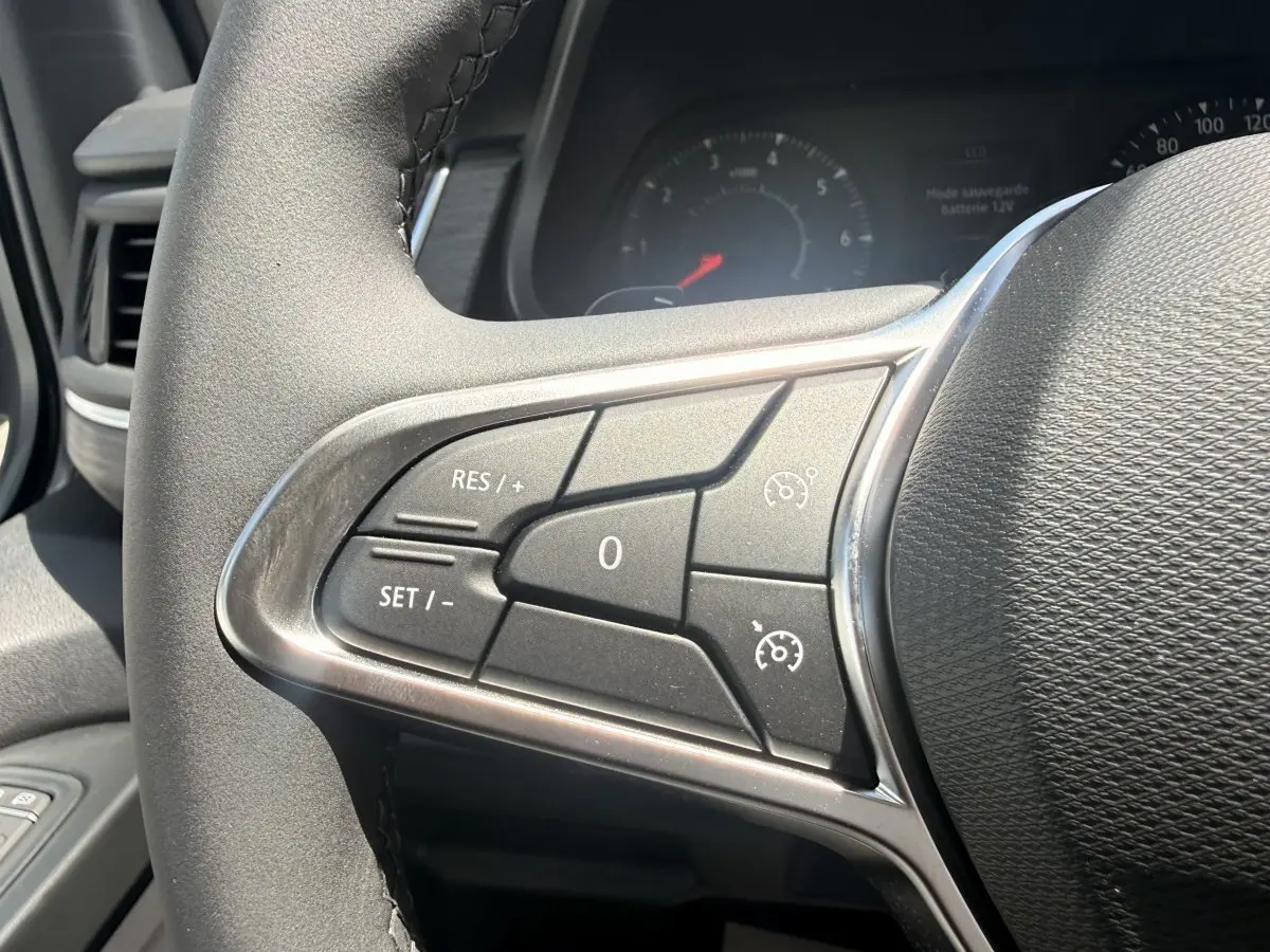 Gros plan sur les commandes du régulateur de vitesse au volant noir du Renault Trafic Fourgon blanc, vue côté gauche.
