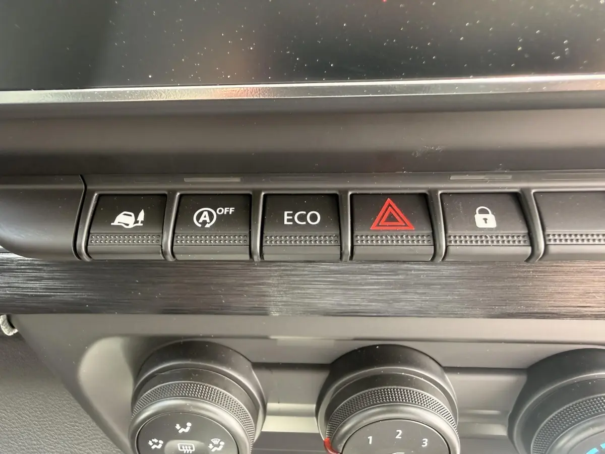 Gros plan sur la rangée de boutons de commande noirs et molettess du tableau de bord du Renault Trafic Fourgon blanc.