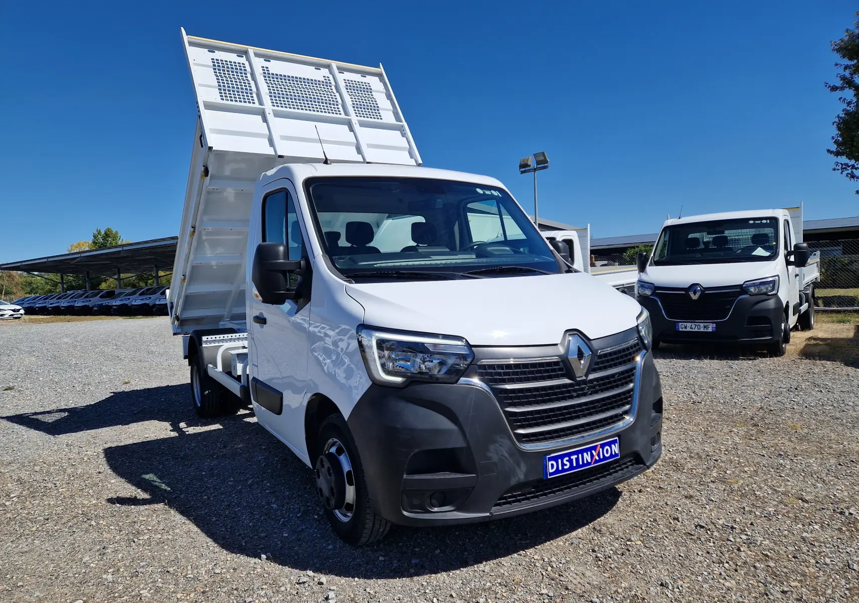 Renault Master Benne blanc vue 3/4 avant droit avec benne relevée et roues jumelées sur sol gravillonné.