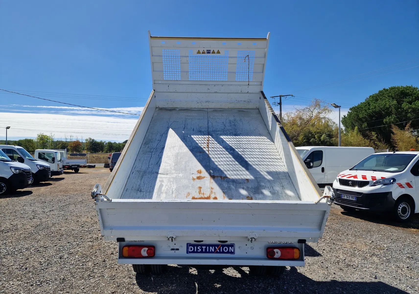 Vue arrière en contre-plongée d’un Renault Master Châssis Cabine blanc avec benne basculée et plateau métallique usé.