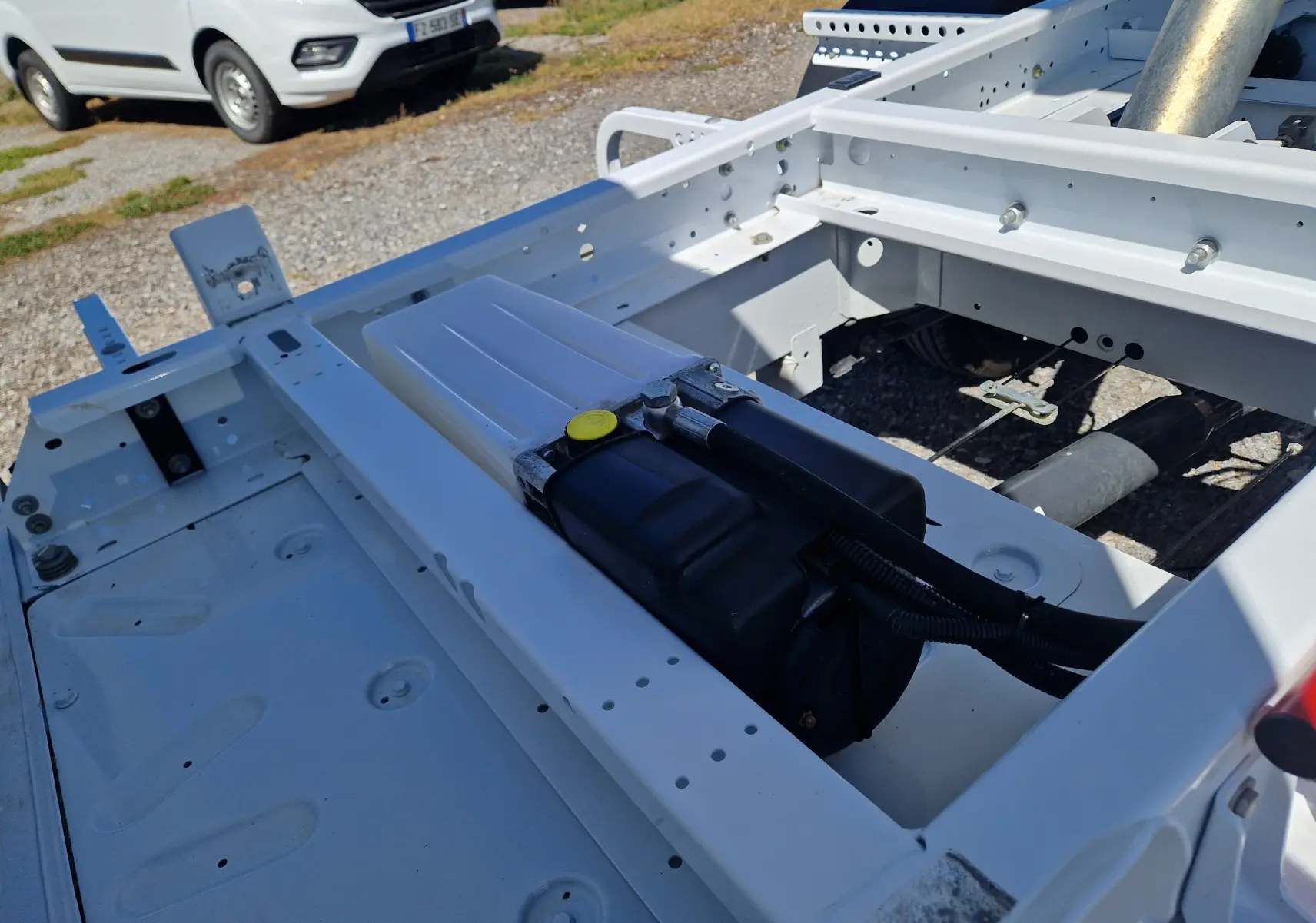 Vue rapprochée du châssis blanc du Renault Master Benne L2, montrant la structure métallique et un réservoir noir intégré.