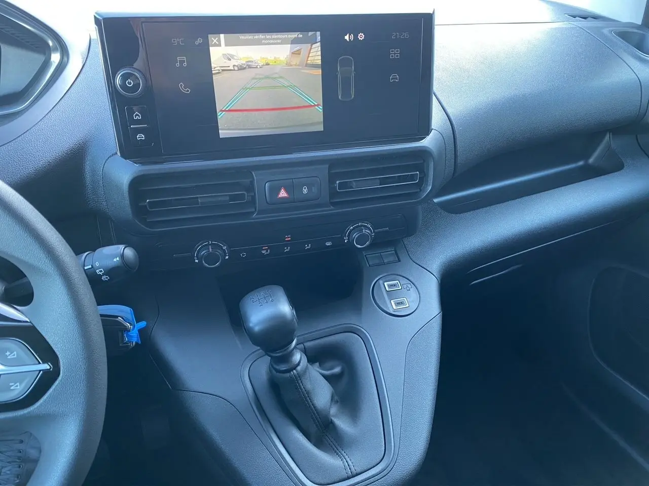 Vue intérieure du tableau de bord du Peugeot Partner blanc 2024, avec écran caméra de recul et levier de vitesses manuel.