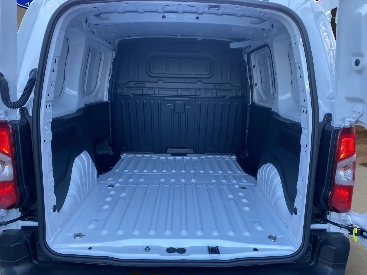 Vue arrière ouverte du Peugeot Partner blanc 2024 montrant la grande zone de chargement métallique vide et les feux arrière rouges.